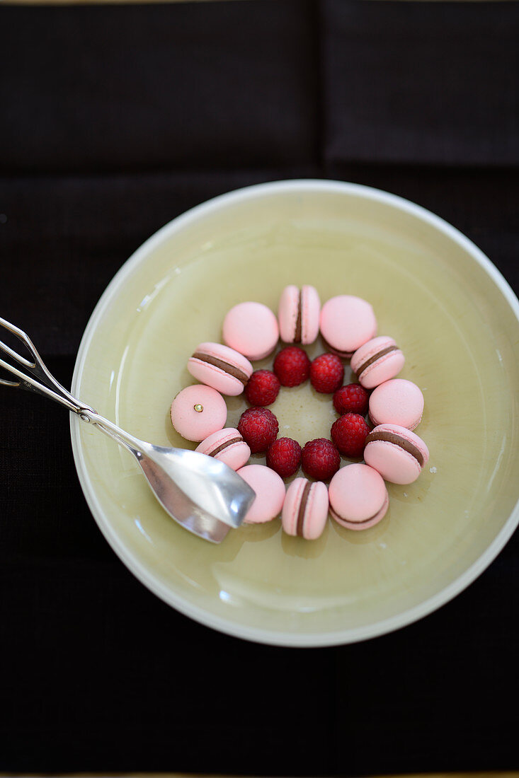 Pink macaroons and raspberries arranged in a circle on a plate