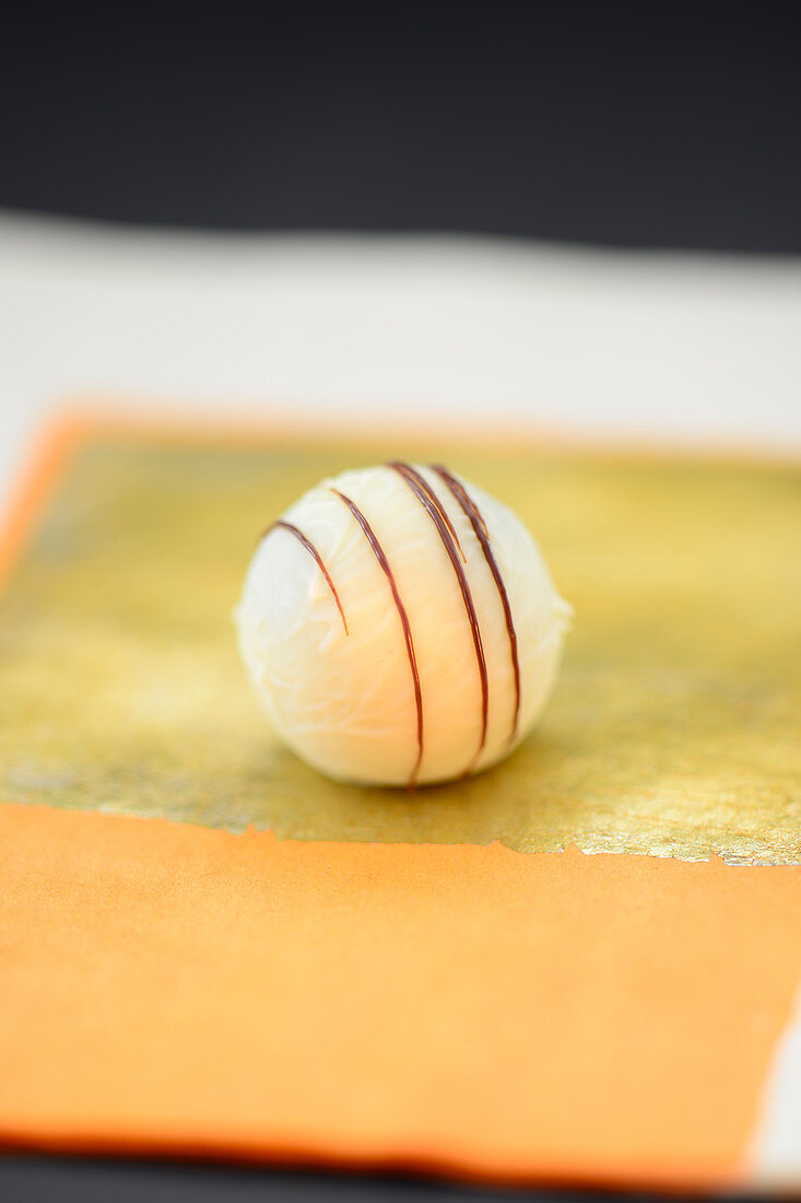 A white truffle praline decorated with fine chocolate stripes