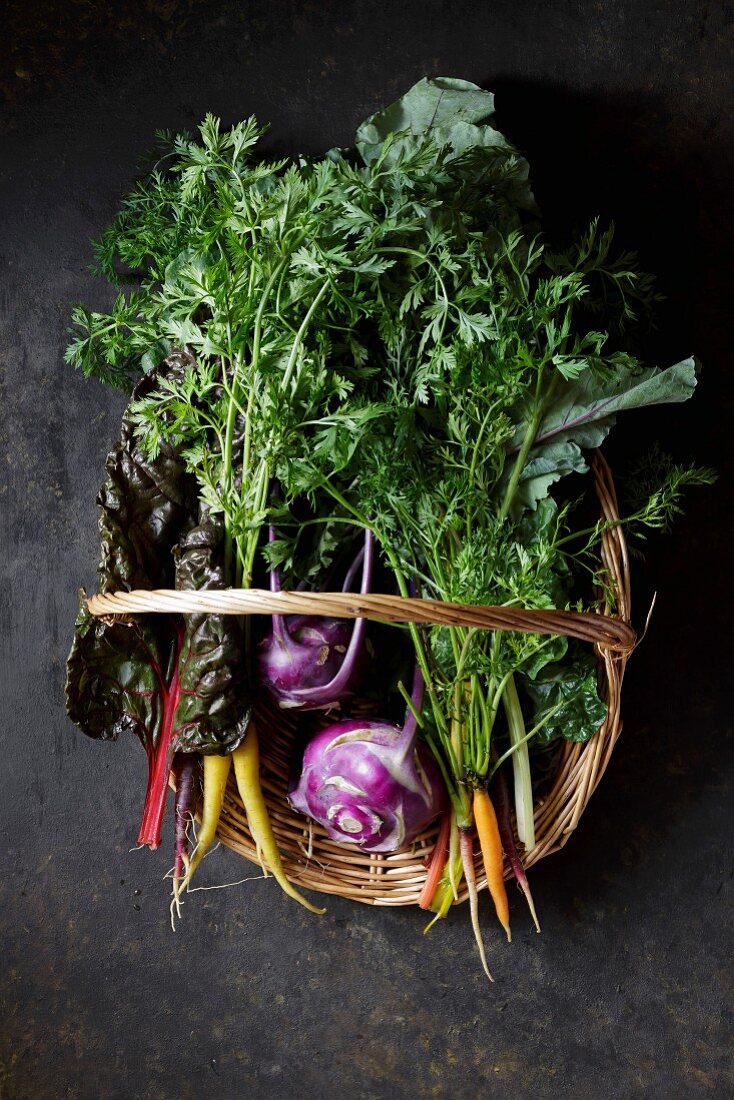Fresh vegetables in a basket, including swiss chard, carrots and Kohlrabi