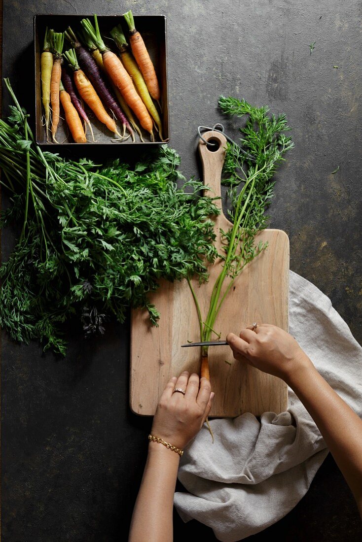 Fresh carrots on a dark background with chopping board and womans hands preparing