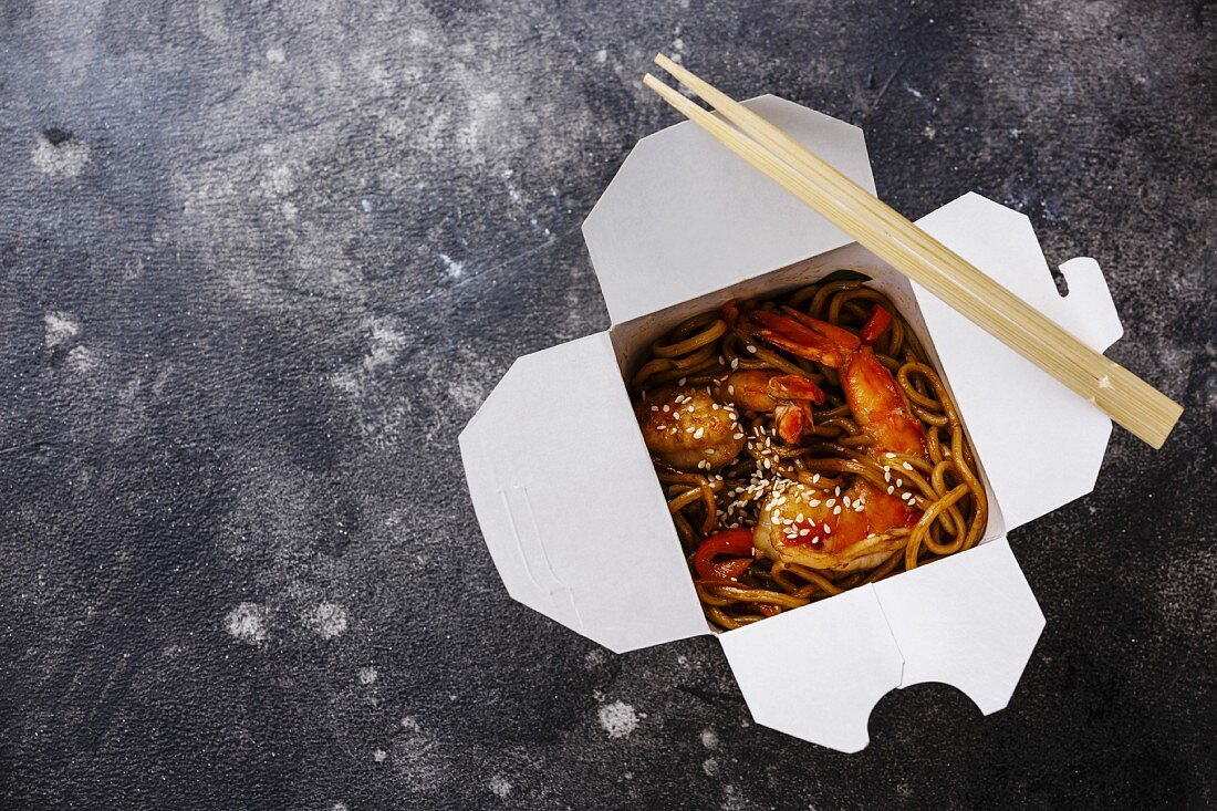 Udon noodles stir-fried with Tiger shrimps Asian food in box Take out food on dark background