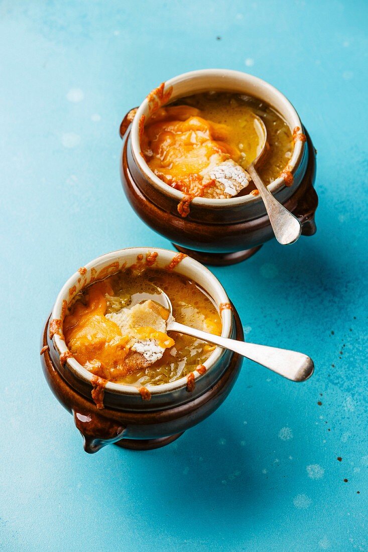 Authentic French Onion soup with dried bread and cheddar cheese in bowl on blue background