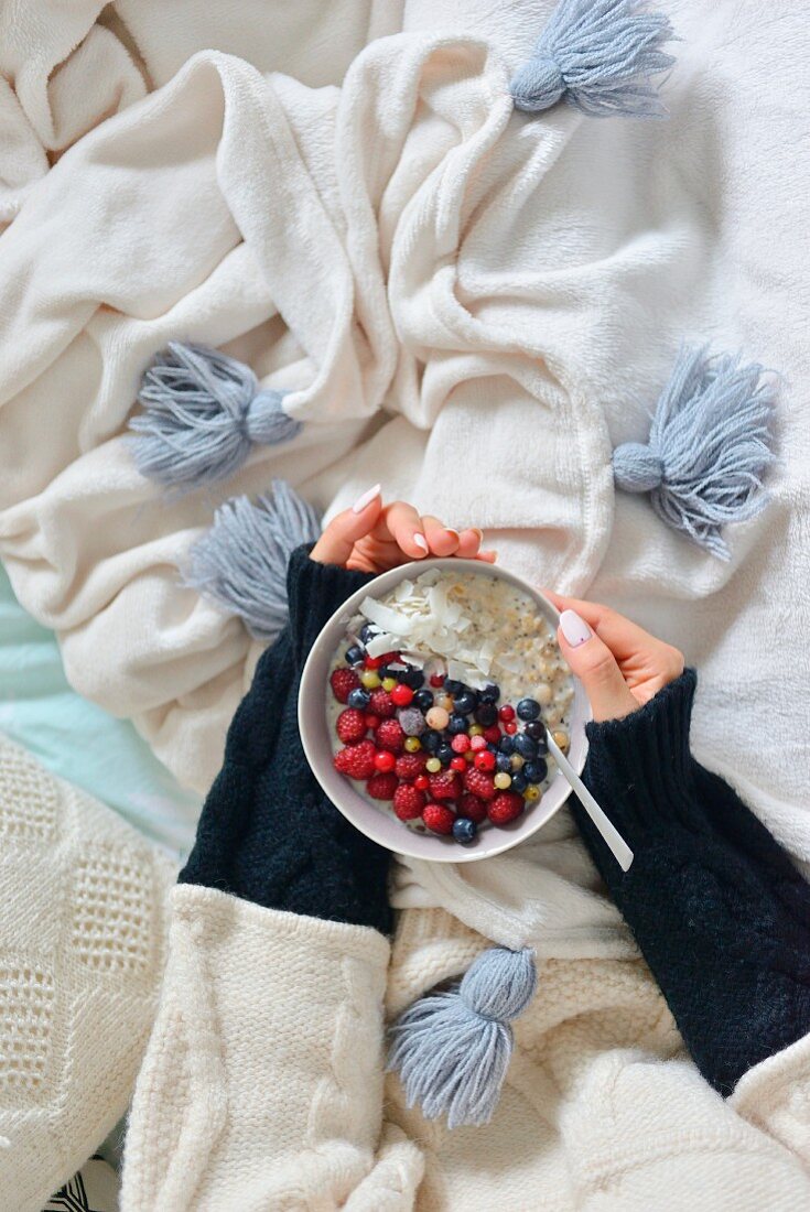 Woman holds a bowl of porridge and fruit in her hands
