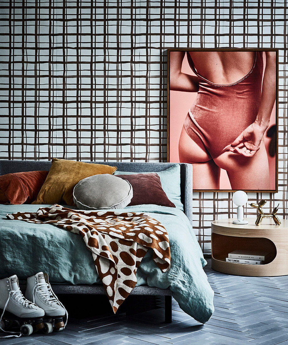 Double bed against wall with wallpaper and large-format photo, next to it round bedside table