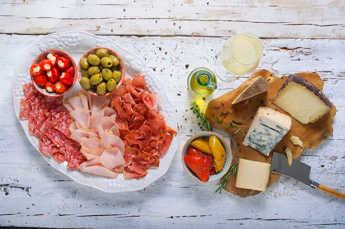 Käse- und Wurstplatte mit Oliven, gefülltem Gemüse und Weißwein
