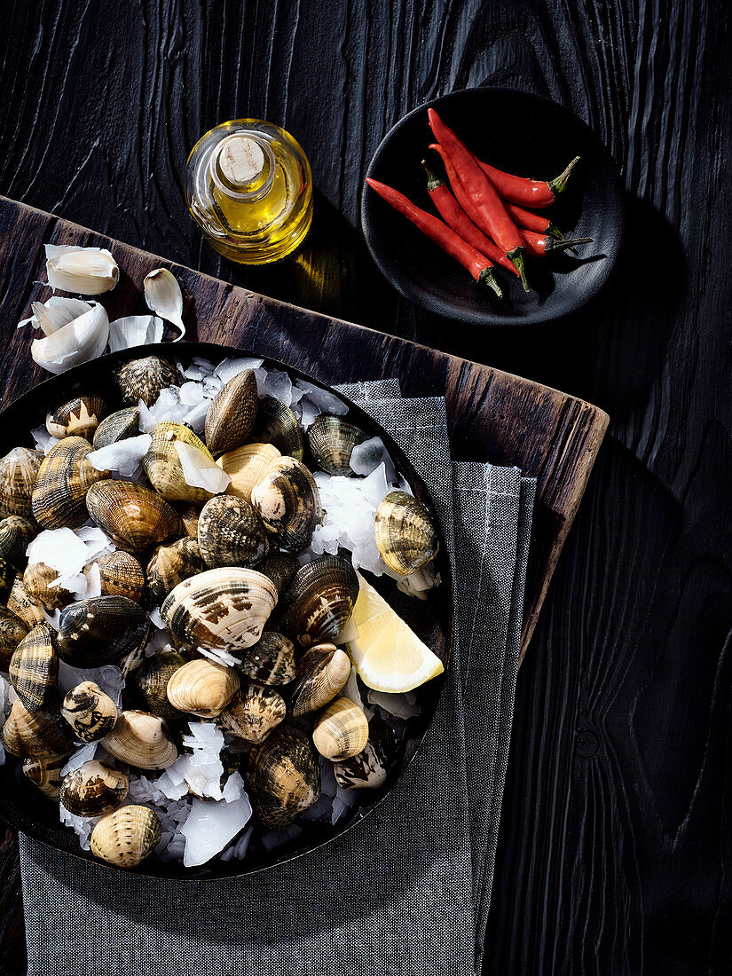 An arrangement of ingredients with fresh clams on ice, chilli and olive oil