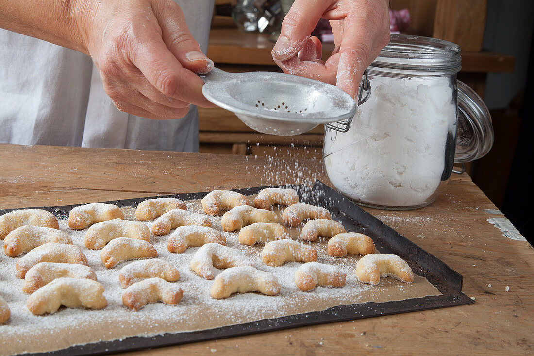 Gluten-free vanilla crescent biscuits being dusted with icing sugar