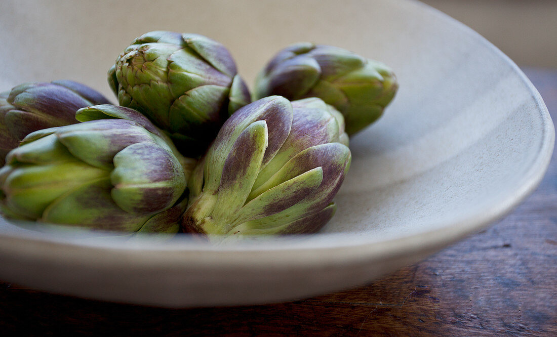 Artichokes in a beige bowl on a wooden table