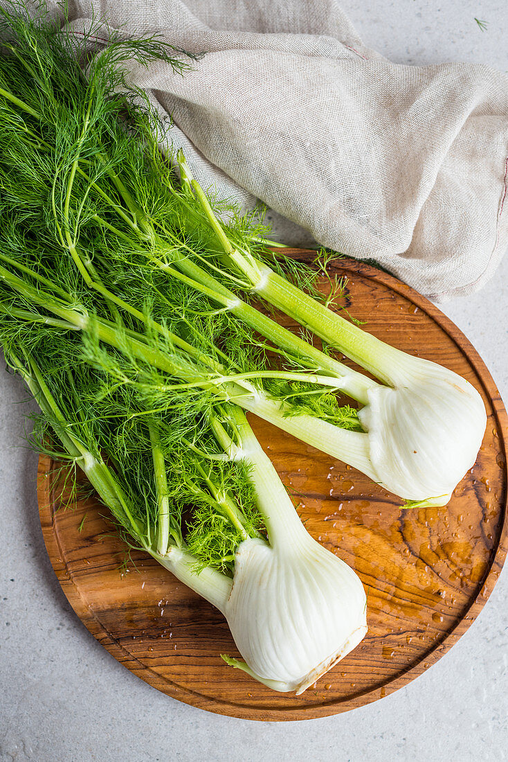 Two bulbs of fennel with leaves on a wooden board