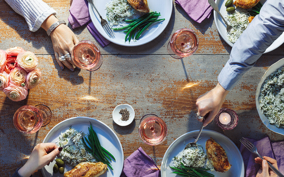 A table scene with chicken, rice, olives, green beans and wine