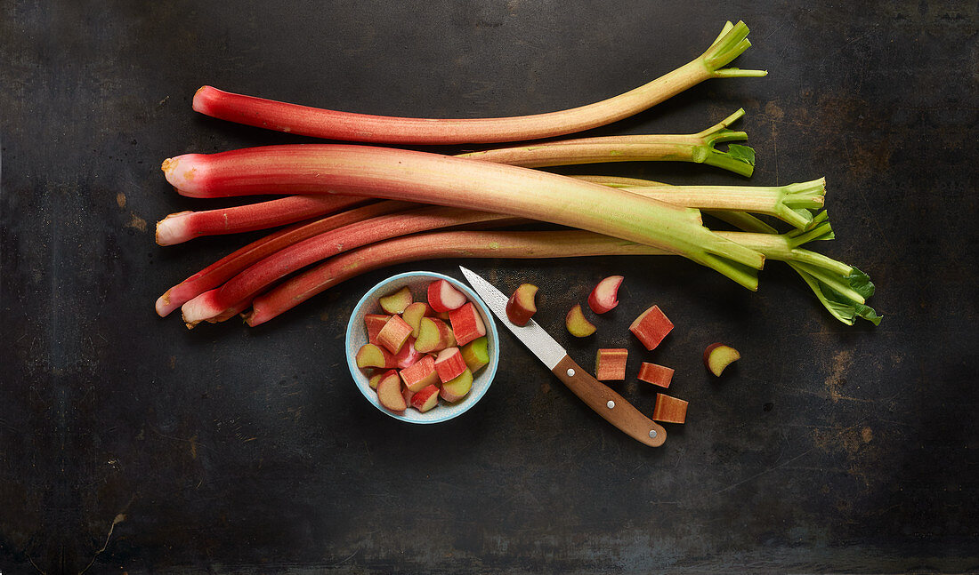 Rhubarb stems and chopped rhubarb in a bowl with a knife