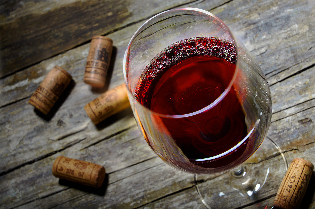 A red wine glass and corks on a rustic wooden table