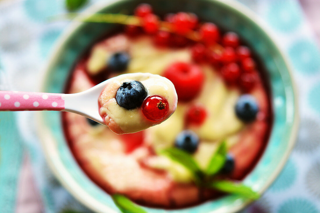 Vanillepudding mit frischen Früchten und Fruchtsirup auf Löffel über Schale