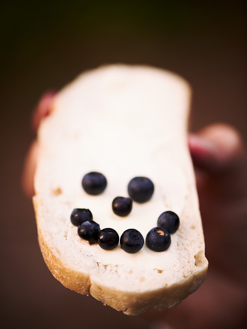 A blueberry smiley on a slice of buttered bread