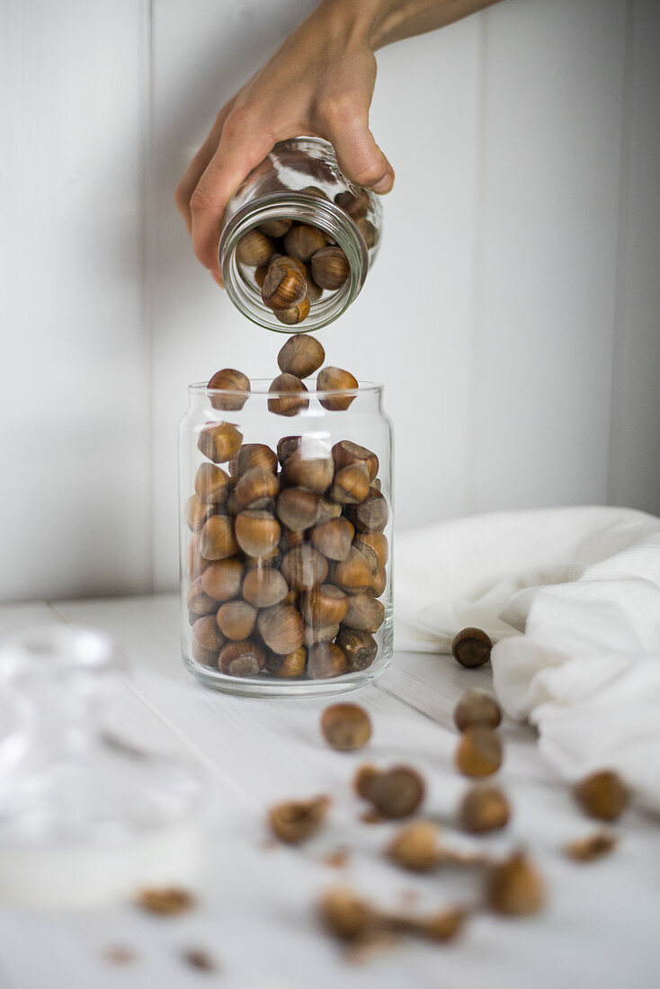 Hazelnuts being poured into a glass storage jar
