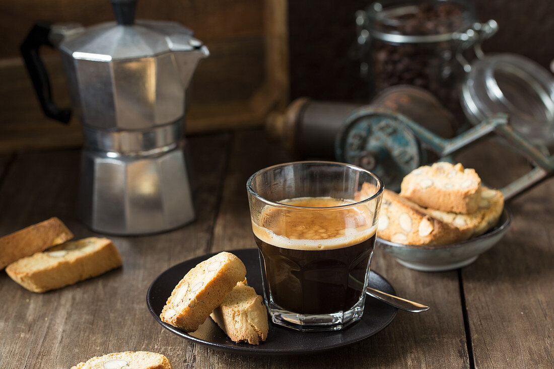 Espresso in a glass and cantuccini with a stove-top coffee maker in the background