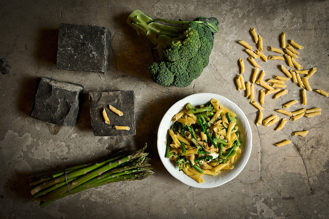 Pasta with broccoli and green asparagus surrounded by ingredients