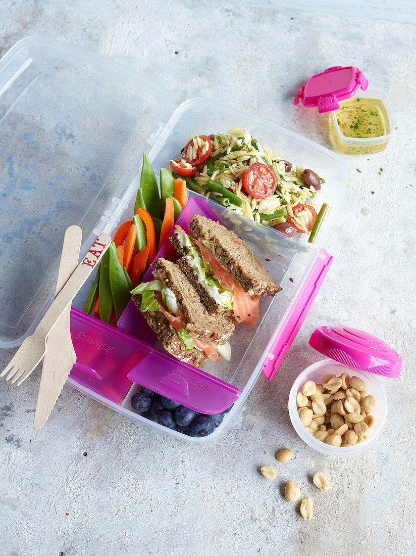 A substantial lunchbox with a pasta salad, vegetable stick and sandwiches