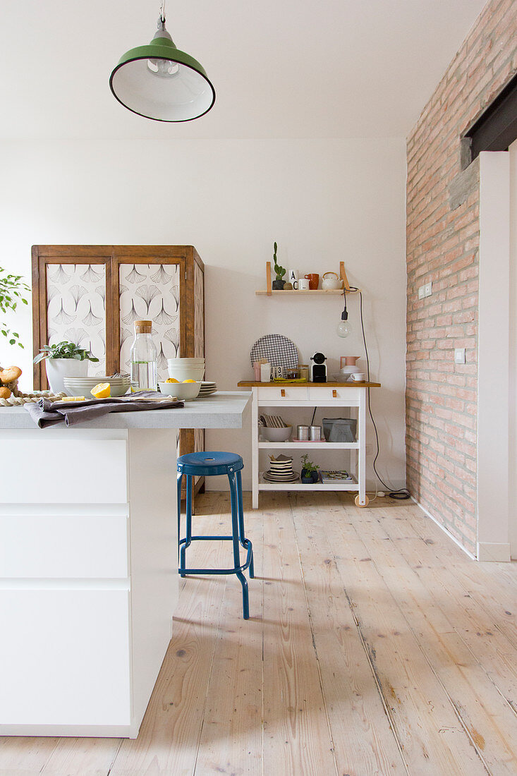 White kitchen island and blue barstool in open-plan kitchen with wooden floorboards and exposed brick wall
