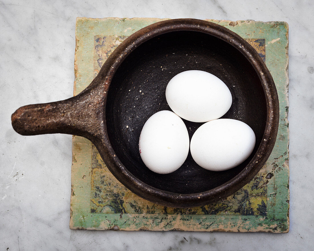 Drei weiße Eier im Keramiktopf