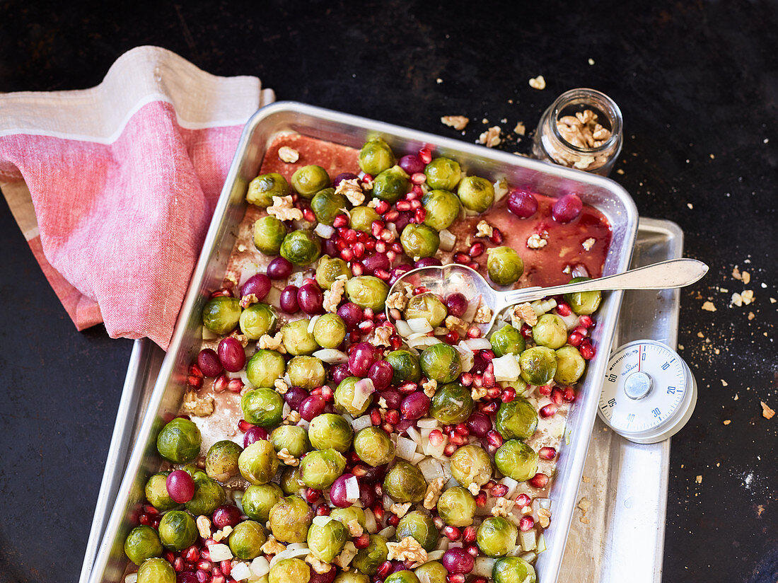 Brussels sprouts and onions on a baking tray with grapes and pomegranate seeds