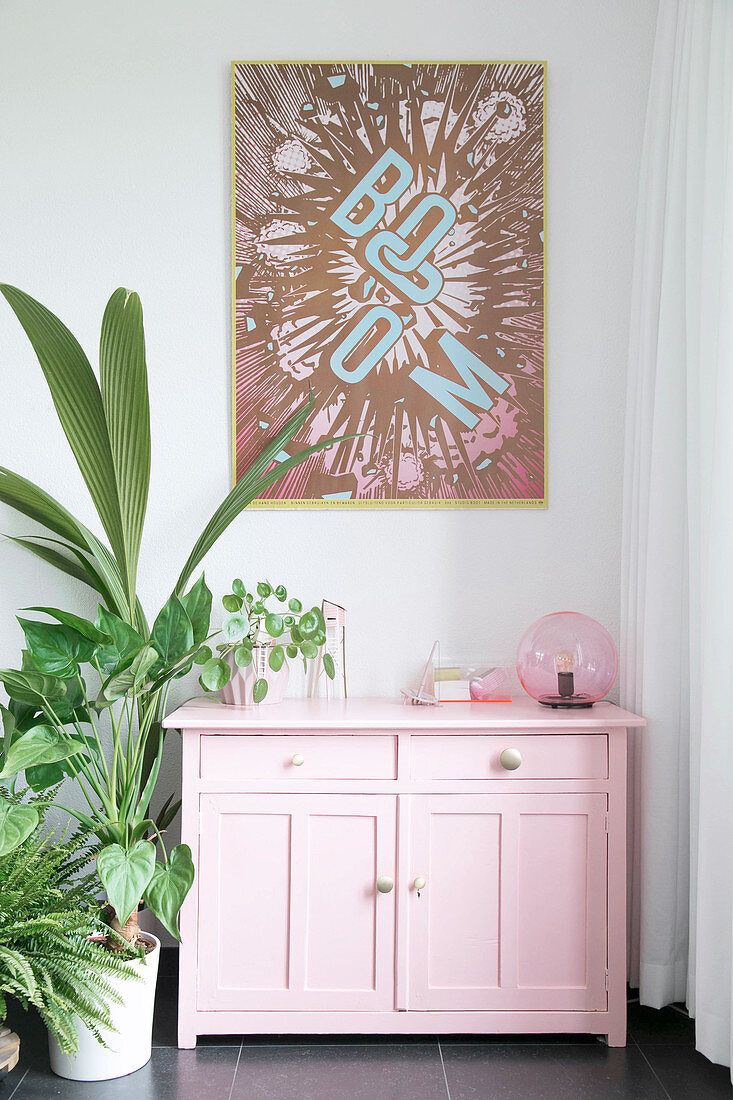 Pop art picture above pink cabinet and houseplants
