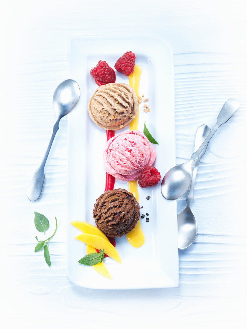 Various ice cream scoops with mango and raspberry sauce