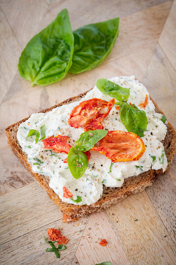 A slice of bread topped with cream cheese, tomatoes and basil