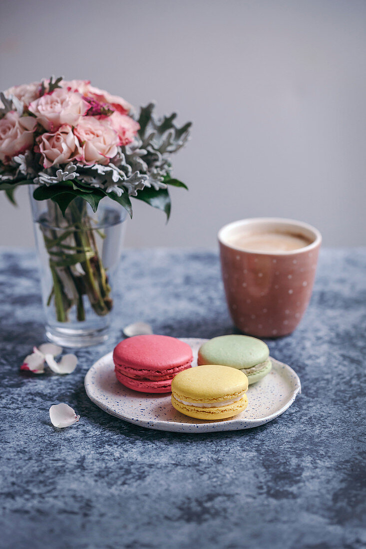 Drei Macarons auf Dessertteller dazu eine Tasse Kaffee