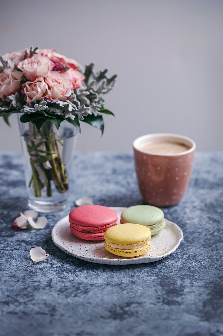 Macarons on a dessert plate and a cup of coffee on grey background