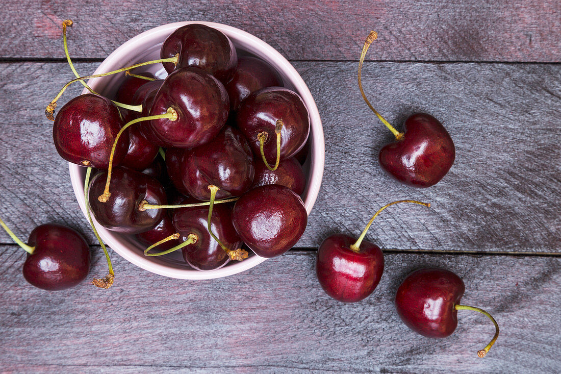 Cherries in a bowl and on a wooden surface (seen from above)