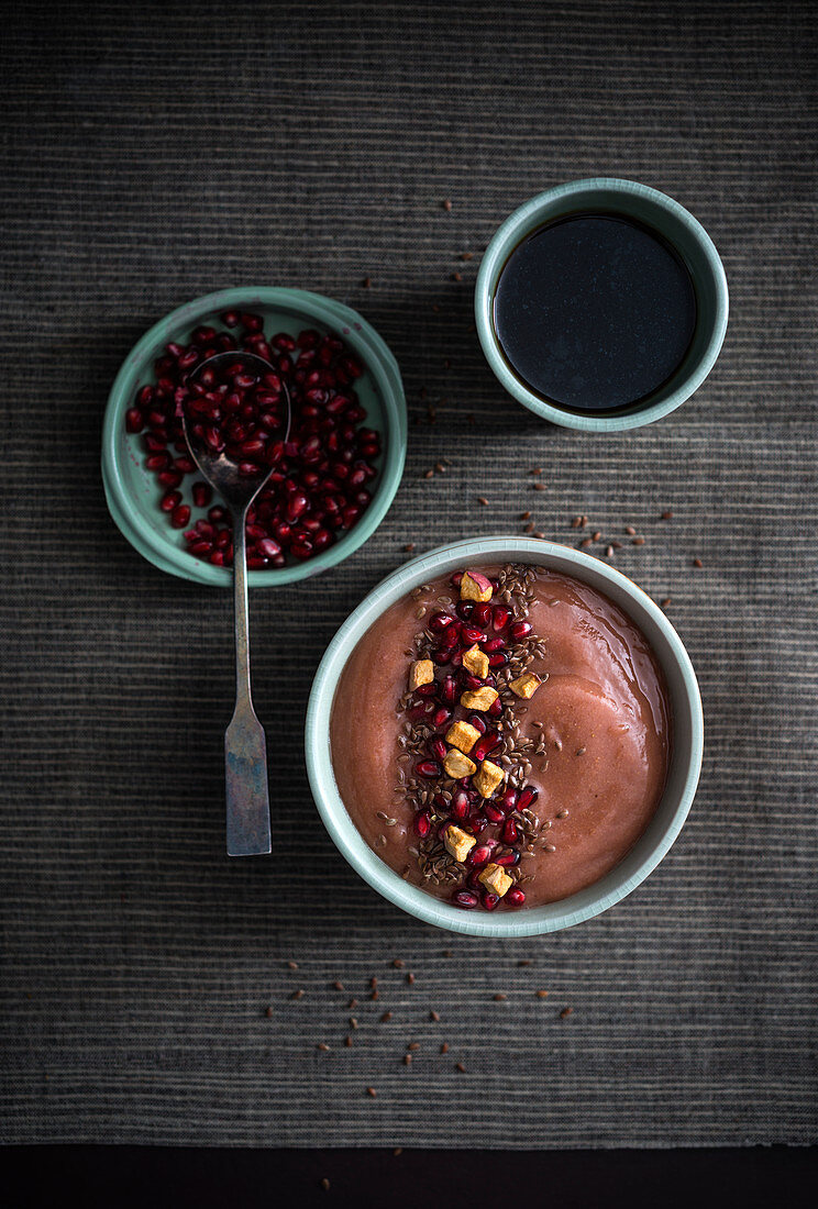 Vegan banana and peanut smoothie bowl with pomegranate seeds, dried apple and flaxseeds