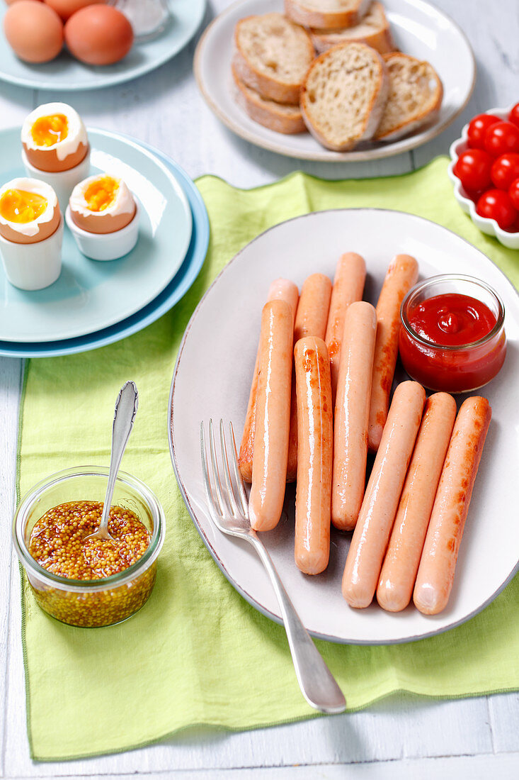 Gekochte Würstchen mit Dips, weichen Eiern und Tomaten zum Frühstück