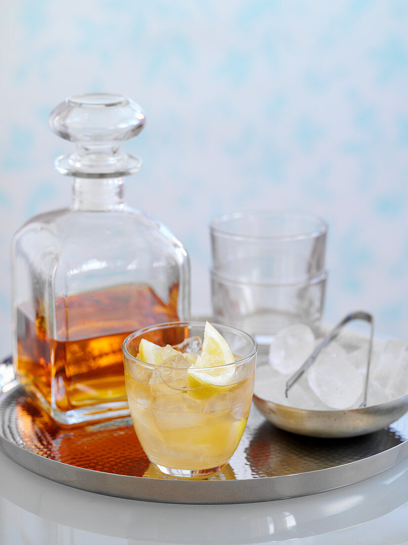 A whiskey cocktail with ice and lemon wedges