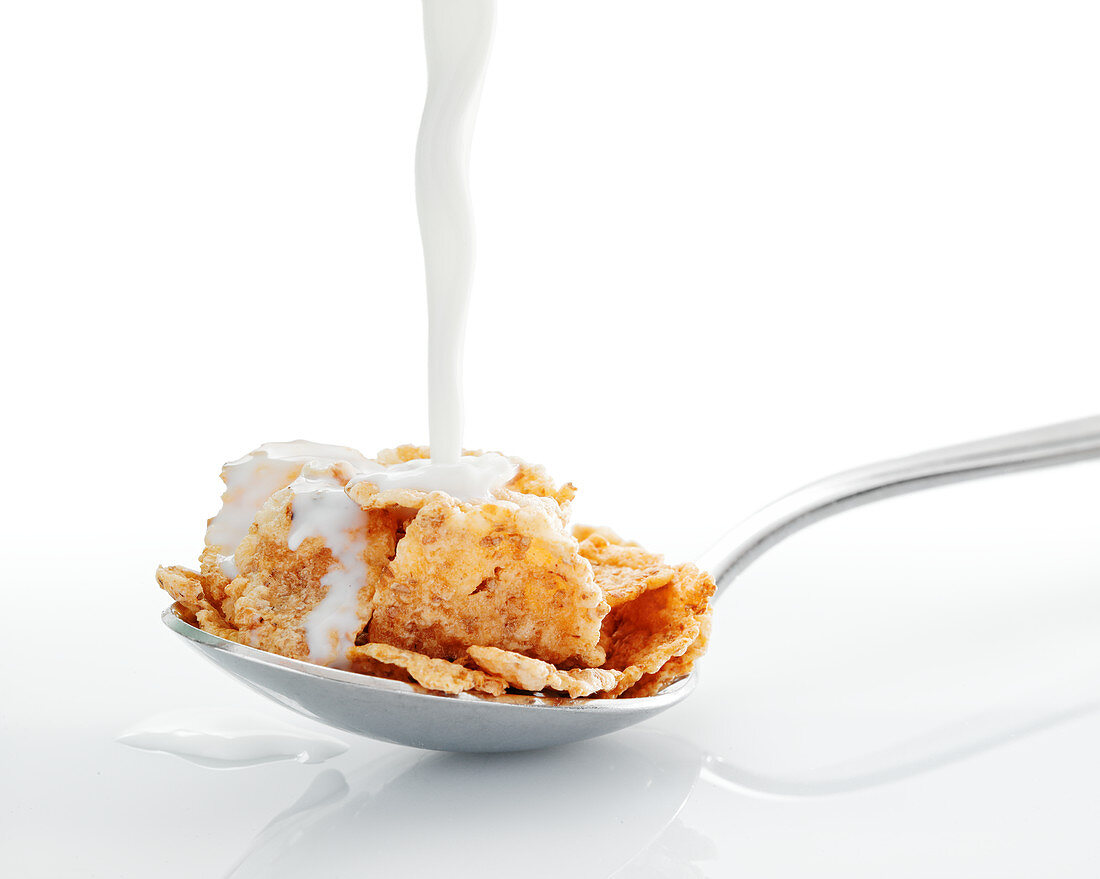 Milch fliesst auf Löffel mit Cornflakes