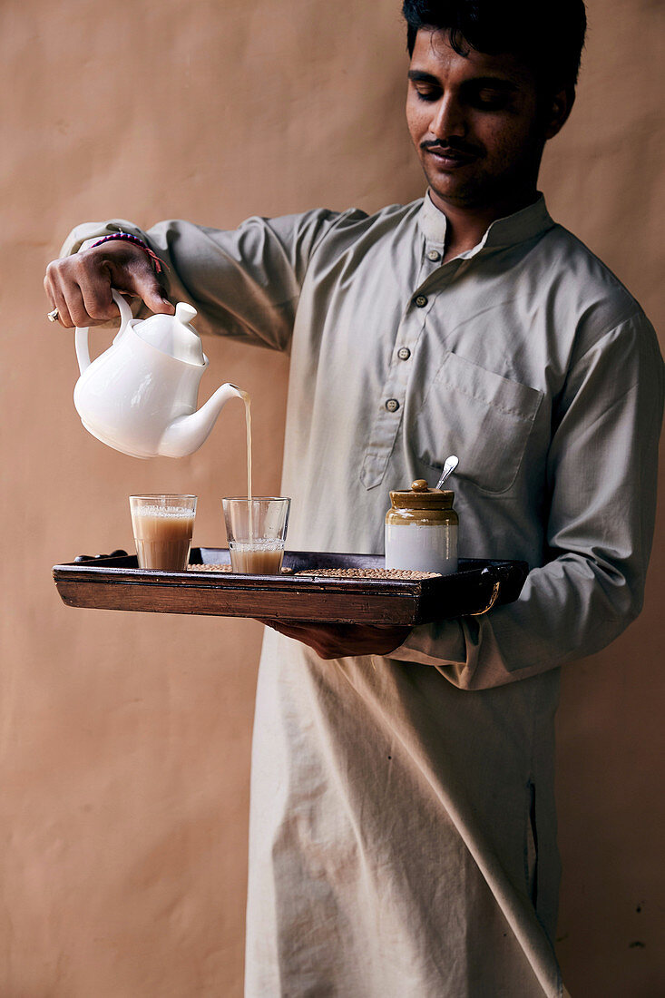 Indischer Kellner gießt Tee in Gläser