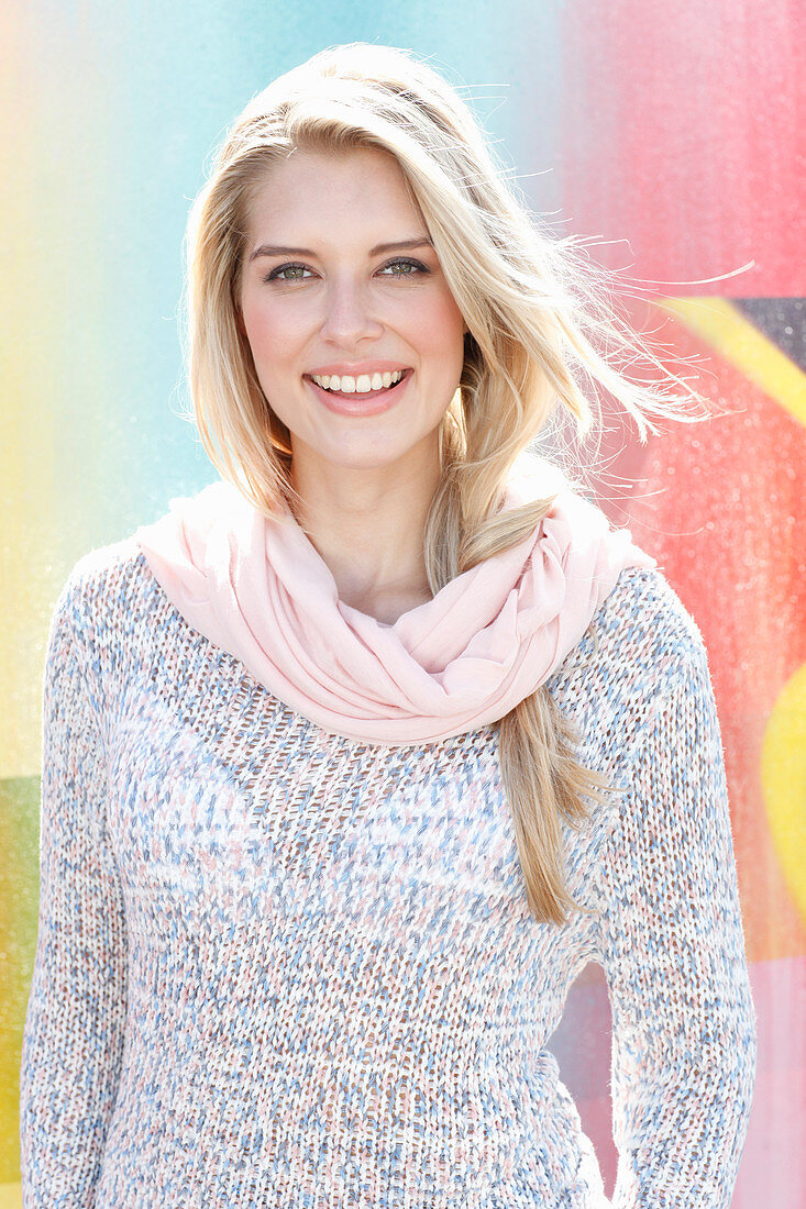 A young blonde woman wearing a knitted jumper and a pink loop scarf