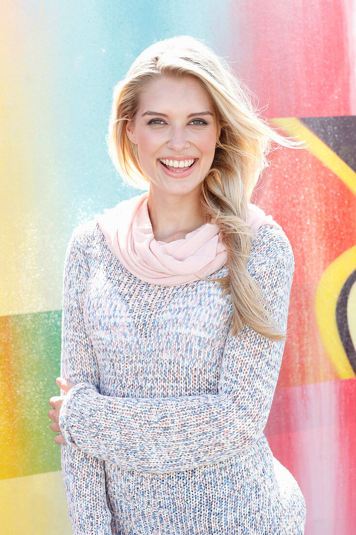 A young blonde woman wearing a knitted jumper and a pink loop scarf