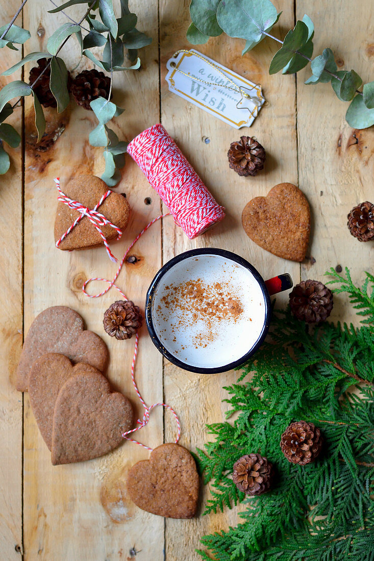 Herzförmige Lebkuchenplätzchen, Kaffeebecher und Weihnachtsdekoration auf einem Holztisch