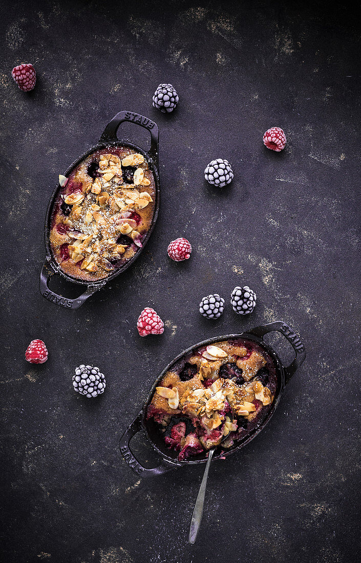 Clafoutis with raspberries, blackberries, flaked almonds, icing sugar and a fork