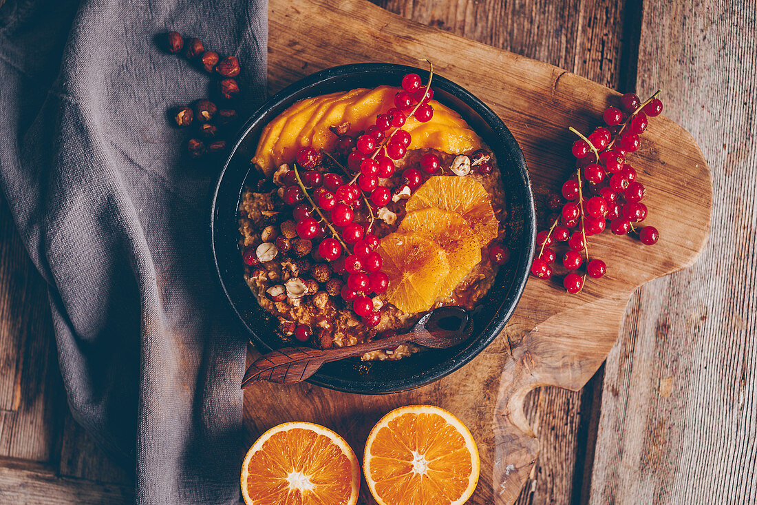Herbstporridge mit Zimt, Haselnüssen, Orangenscheiben, roten Johannisbeeren und Mango