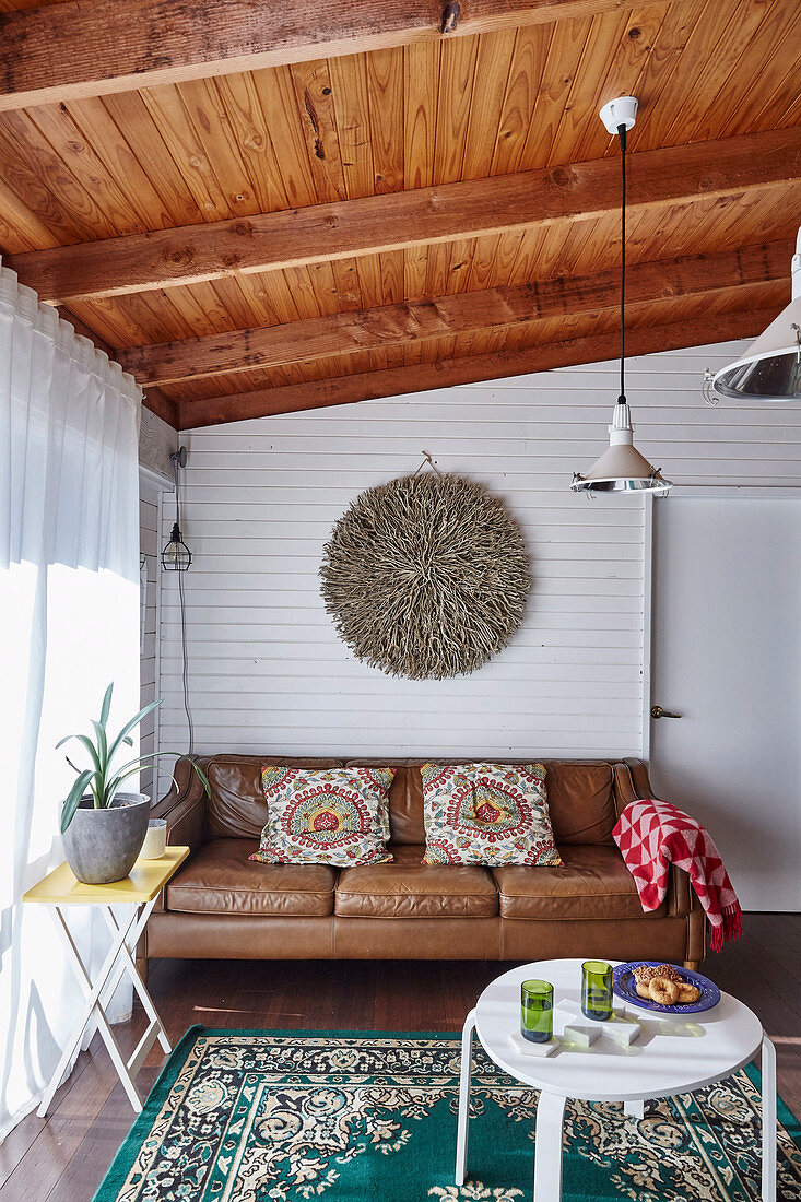 Braune Ledercouch und weißer Tisch im Wohnzimmer mit Holzbalkendecke