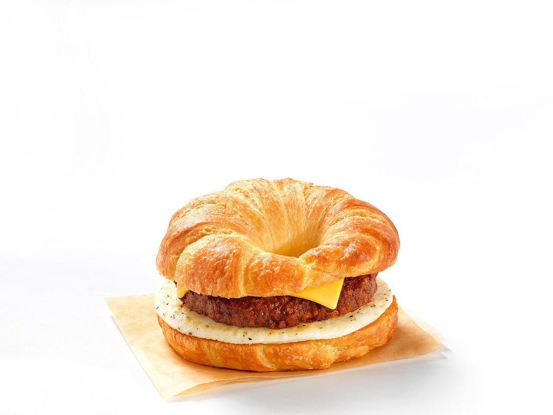 A croissant burger with cheese and egg against a white background