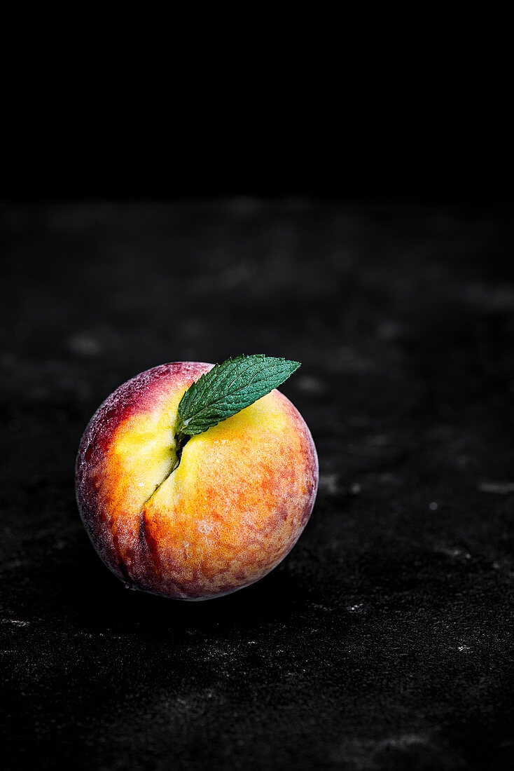 A peach with a leaf on a dark background