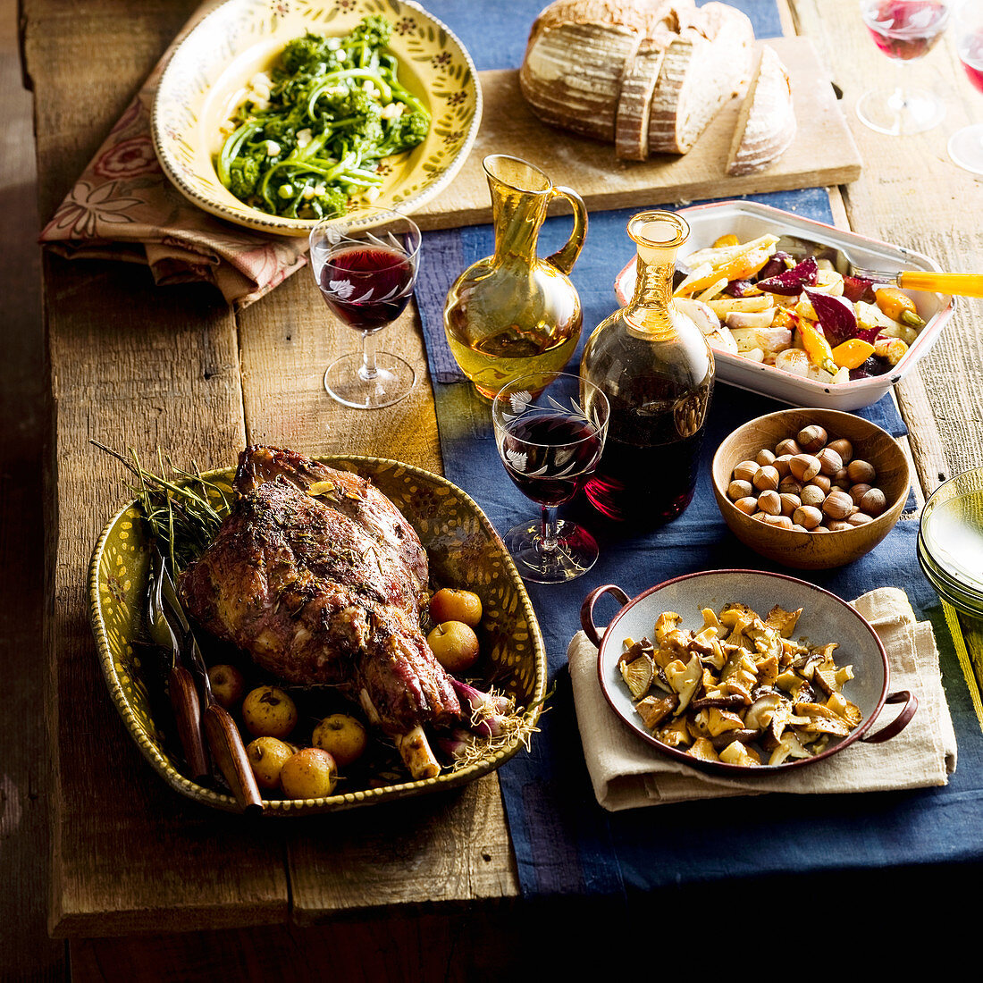 A table laid with a roasted leg of lamb, mushrooms, vegetables and wine