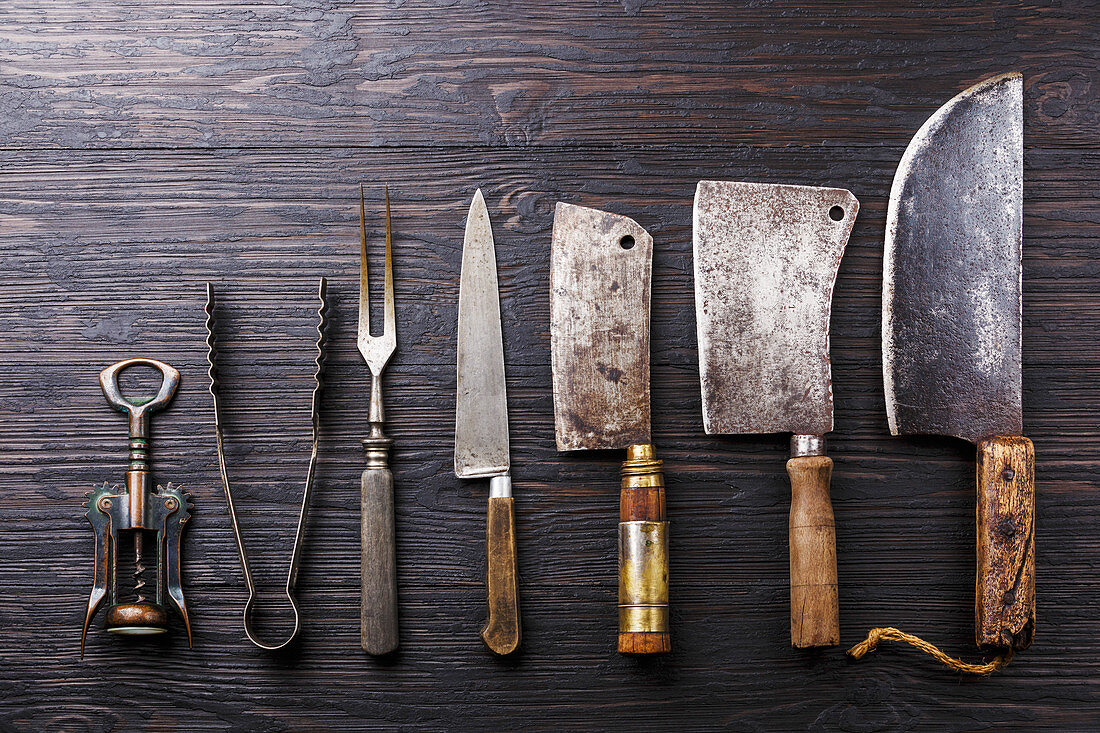 Vintage Butcher meat cleavers, corkscrew and tongs on dark burned wooden background