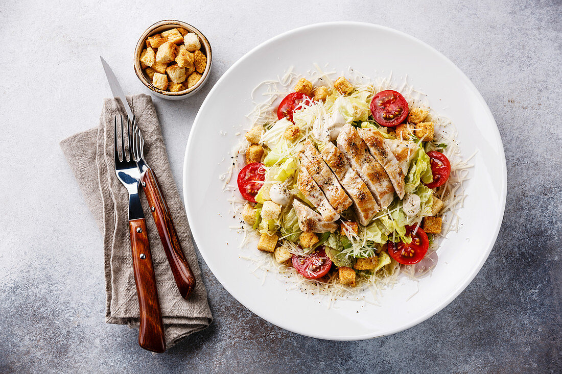 Caesar salad with chicken breast and croutons on gray background
