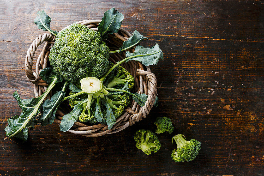 Raw broccoli in basket on wooden table background