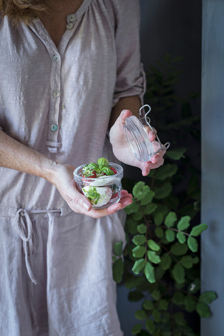 A woman holding a jar of strawberry salad with mozzarella cheese