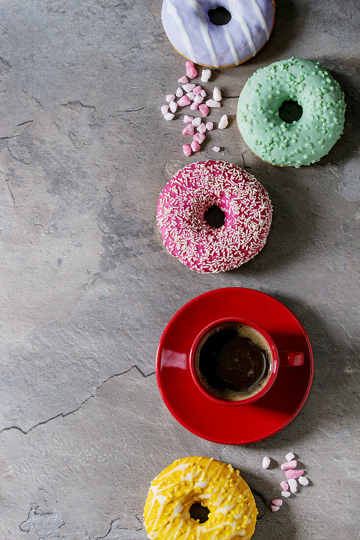 Variety of colorful glazed donuts with pink sugar and red cup of black coffee